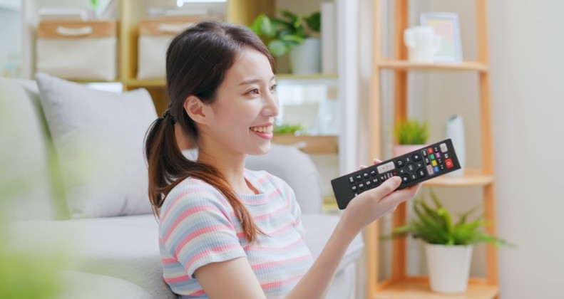 リモコン操作しテレビを見る女性