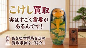 伝統的な和室を背景に、金と深紅の文字で「こけし買取」「あきなや群馬支店」と書かれたサムネイル。中央の座卓には、伊勢と吉田多加志による緑と金の扇模様の木目込みこけしと、その銘板2枚、茶器、扇子が並べられている。下部には「一点一点を丁寧に査定させていただきます」とあり